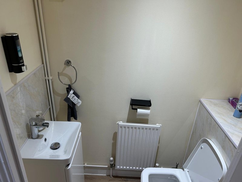 Compact bathroom with white sink, radiator, toilet, and shower enclosure