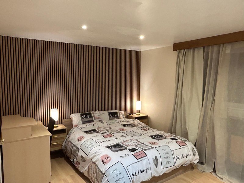 Modern bedroom with double bed, patterned duvet, bedside lamps and floor-to-ceiling curtains