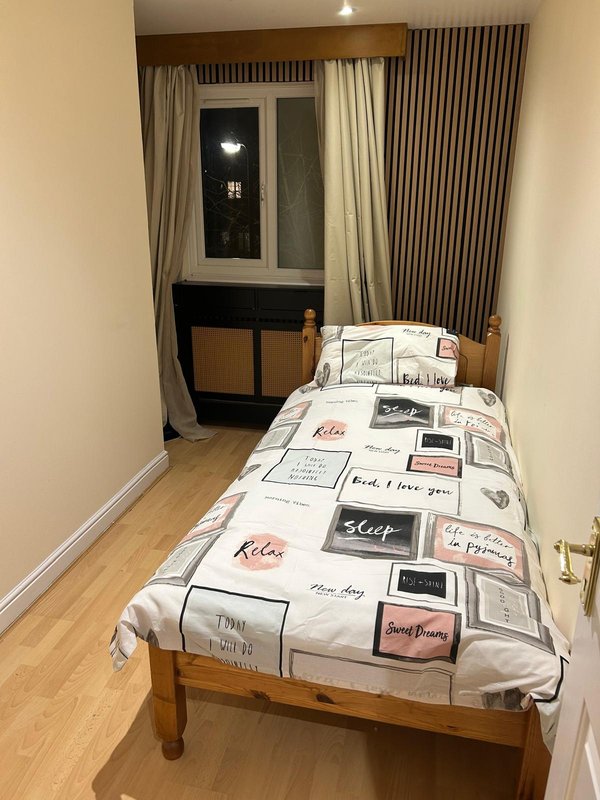 Bedroom with single bed, wooden frame, patterned duvet, window with curtains and door