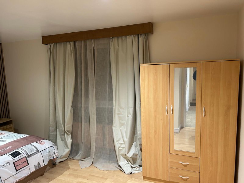 Bedroom with wooden wardrobe, curtained window, and patterned bedding on left