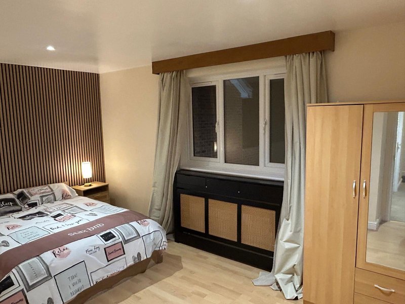 Bedroom with double bed, wooden wardrobe, black dresser, and large window with curtains