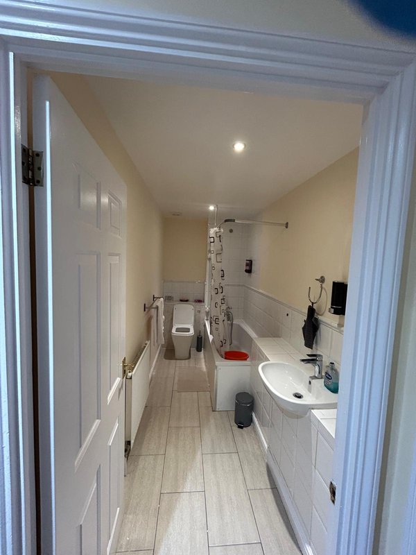 Narrow bathroom with toilet, sink, shower enclosure and white cabinetry