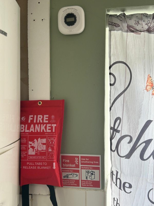Wall-mounted fire blanket and smoke detector in hallway with green painted wall
