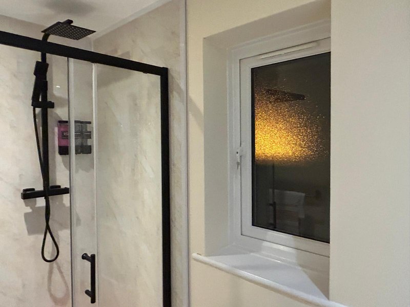 Modern bathroom with walk-in shower, black fixtures, and window with warm lighting