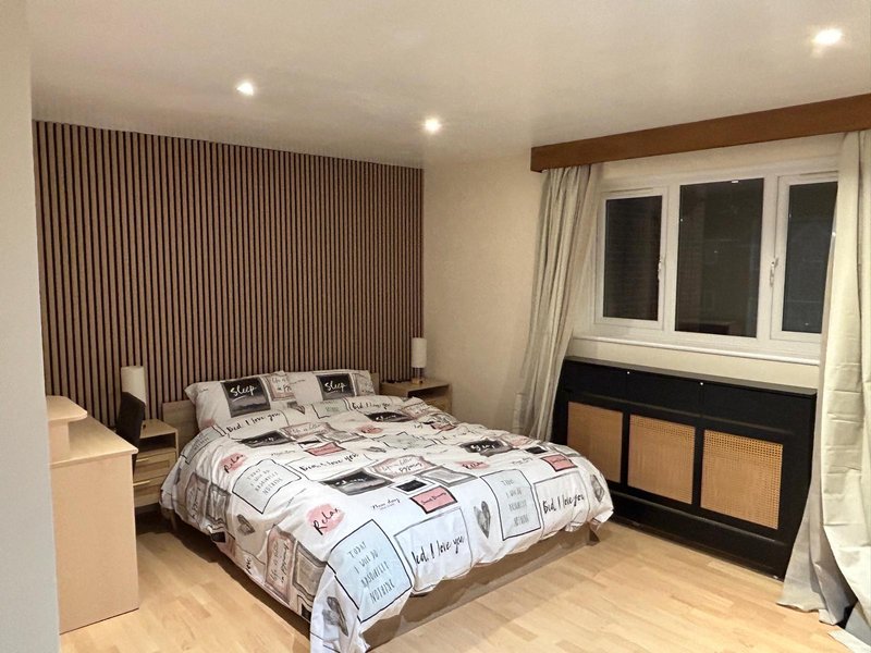 Modern bedroom with double bed, wooden flooring, feature wall paneling and glass doors