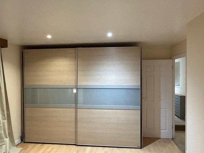Bedroom with large modern sliding wardrobe, wooden flooring and recessed ceiling lights