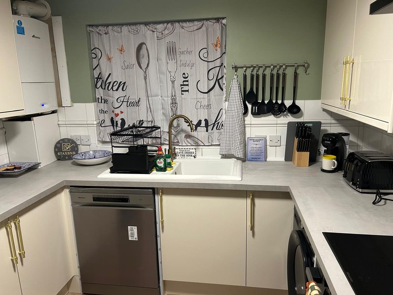 Modern kitchen with white cabinets, countertop appliances, and kitchen-themed window curtain