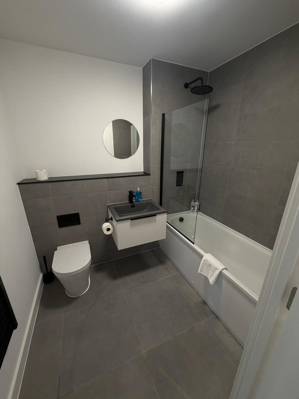 Modern bathroom with toilet, vanity sink, circular mirror, and shower enclosure