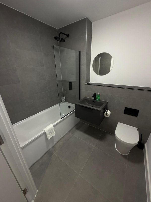 Modern bathroom with walk-in shower, toilet, sink, round mirror and dark tile flooring