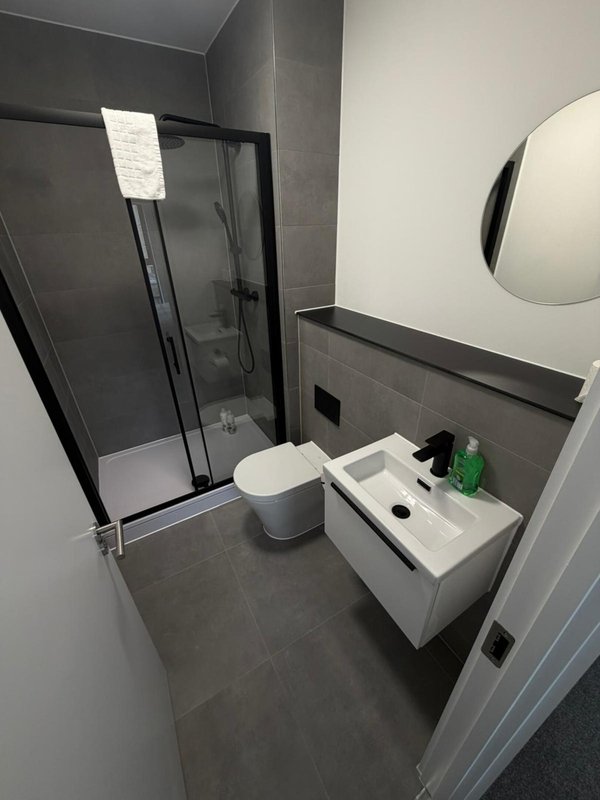 Modern bathroom with shower enclosure, white toilet, sink vanity and round mirror