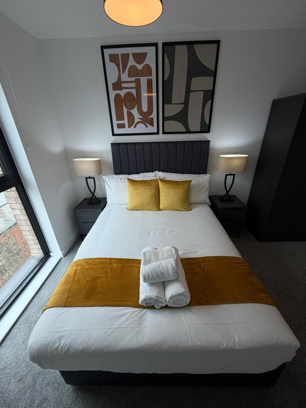 Modern bedroom with double bed, black headboard, yellow pillows and gold throw blanket