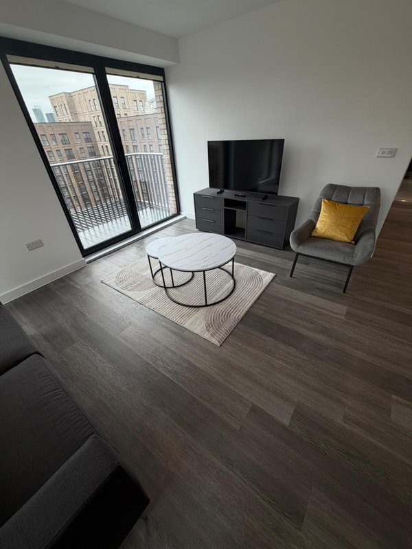 Modern living room with TV unit, armchair, coffee table and large window overlooking city buildings