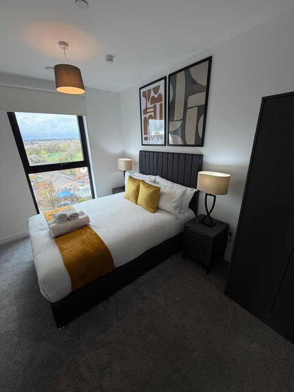 Modern bedroom with double bed, yellow accent pillows, bedside lamps, and city view window