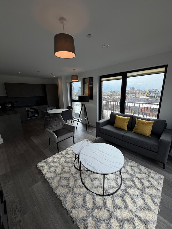 Modern apartment living room with black sofa, pendant light, and city views from balcony