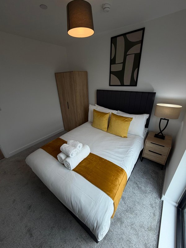 Modern bedroom with double bed, yellow cushions, white bedding, wooden headboard and pendant light