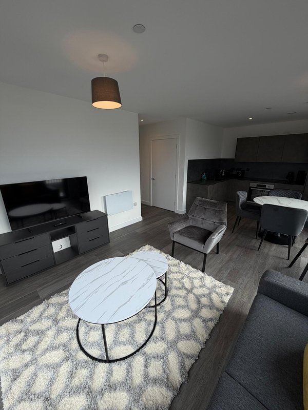 Modern open-plan living area with TV, sofa, white coffee table and kitchen visible