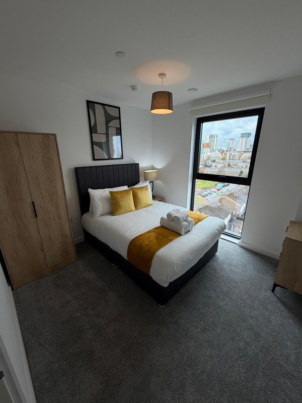 Modern bedroom with double bed, gold cushions, pendant light and city view from window