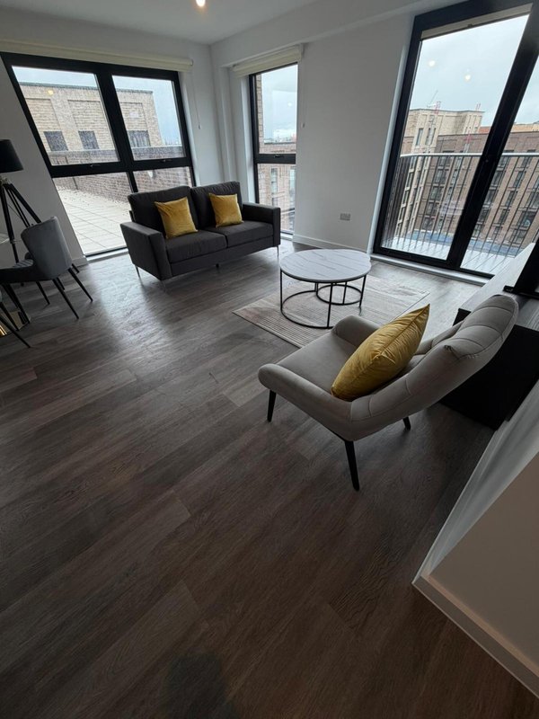 Modern apartment living room with dark sofa, armchair, glass table and floor-to-ceiling windows overlooking city