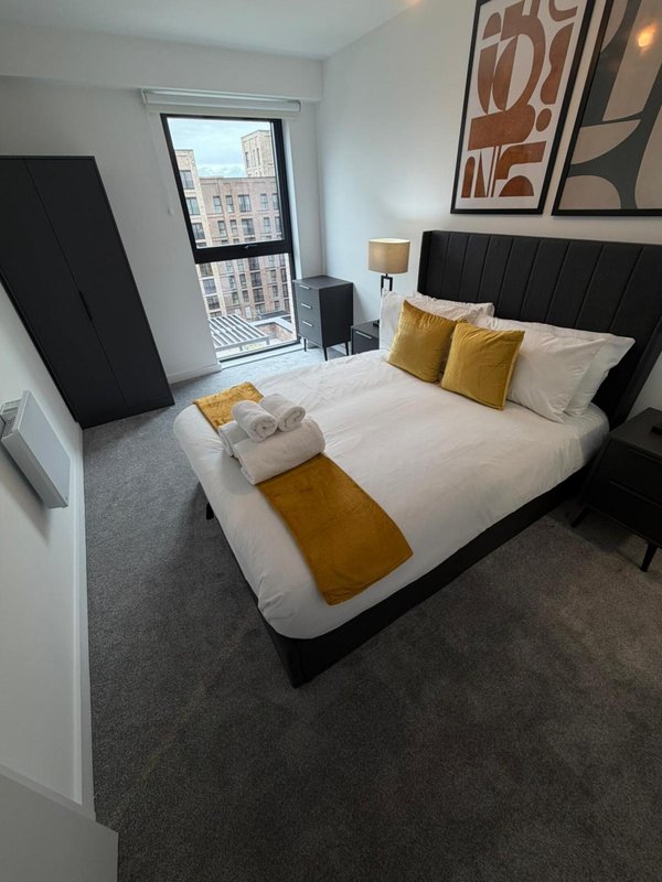 Modern bedroom with black upholstered bed, white bedding, yellow cushions and city view window