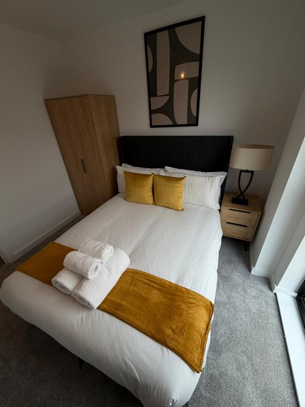 Modern bedroom with double bed, yellow cushions, wooden wardrobe and bedside table