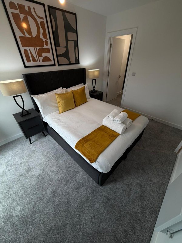 Modern bedroom with black bed frame, white bedding, gold cushions, side table, and abstract wall art