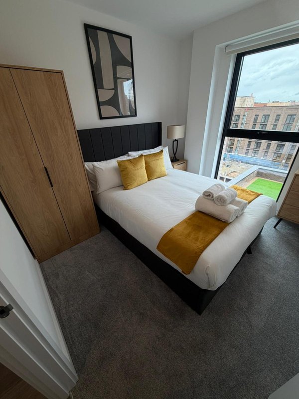 Modern bedroom with double bed, gold cushions, wooden wardrobe and city views from window
