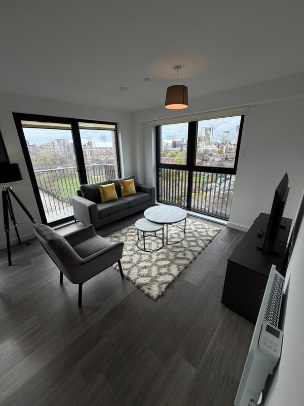 Modern living room with black sofa, armchair, geometric rug and floor-to-ceiling windows overlooking city skyline