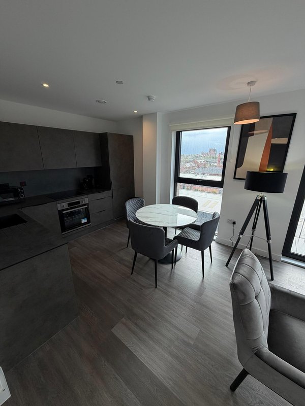 Modern open-plan apartment with kitchen, dining table, and city view from large window