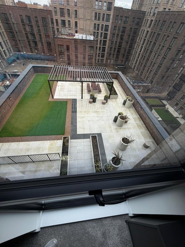 Aerial view of rooftop terrace with paved seating area, green lawn, and surrounding urban buildings