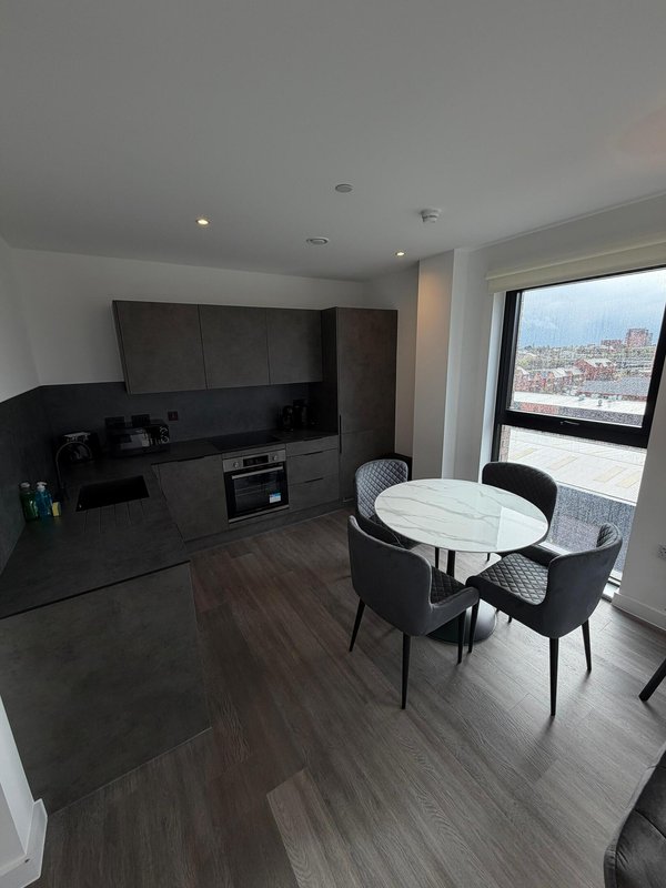 Modern open-plan kitchen and dining area with black cabinetry, round white table, and city view from balcony