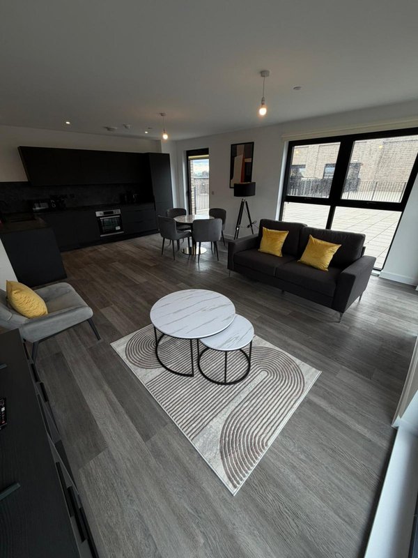 Open-plan living room with black sofa, TV, dining table, wooden flooring and large windows