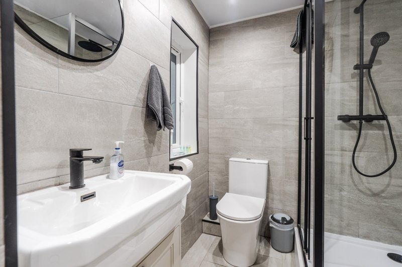 Modern bathroom with white sink, mirror, toilet, shower enclosure and tiled walls