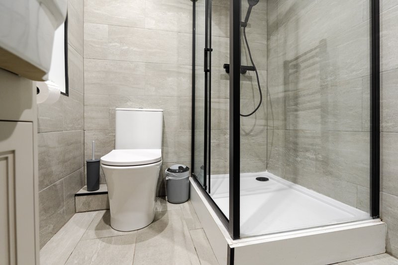 Modern bathroom with toilet, walk-in shower enclosure, and light tile walls