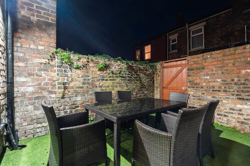 Enclosed brick courtyard with dining table, rattan chairs and artificial turf at night