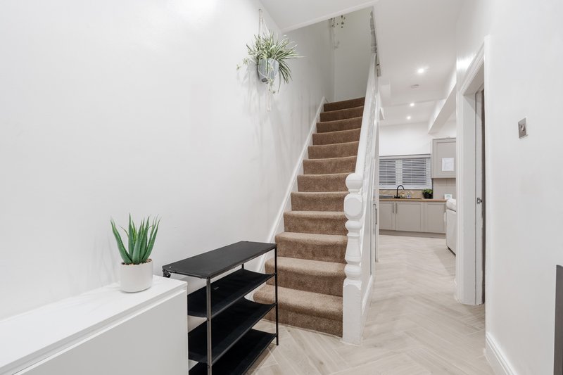 Modern hallway with wooden staircase, white walls, black shelf unit and potted plants