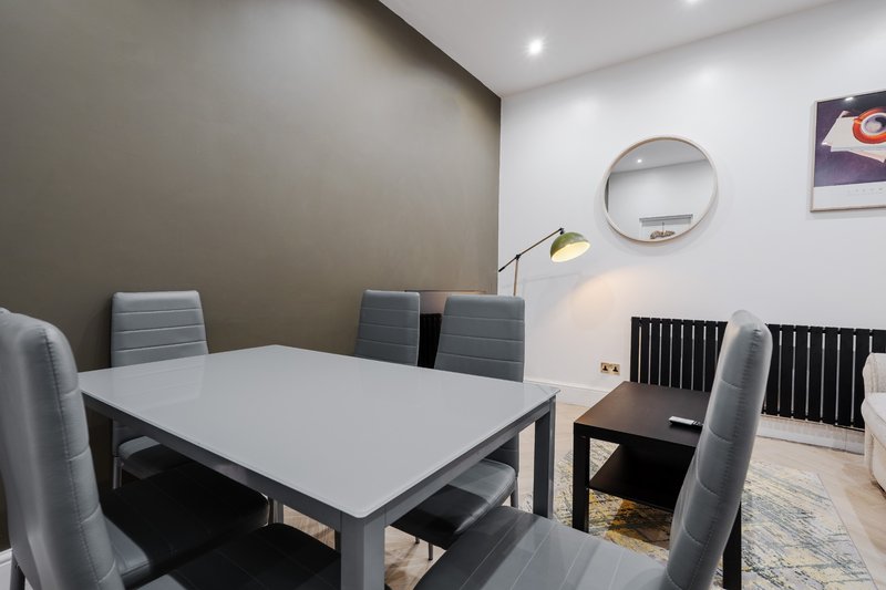 Modern dining room with white table, grey upholstered chairs, wall mirror and pendant lighting
