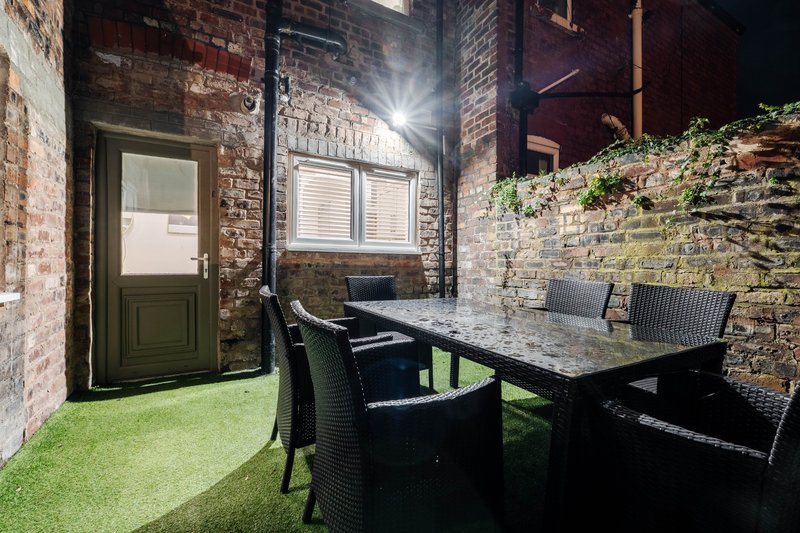 Outdoor courtyard with artificial grass, black dining table, chairs, and brick walls