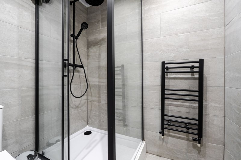 Modern bathroom with walk-in shower, white tray, black fixtures and heated towel rail