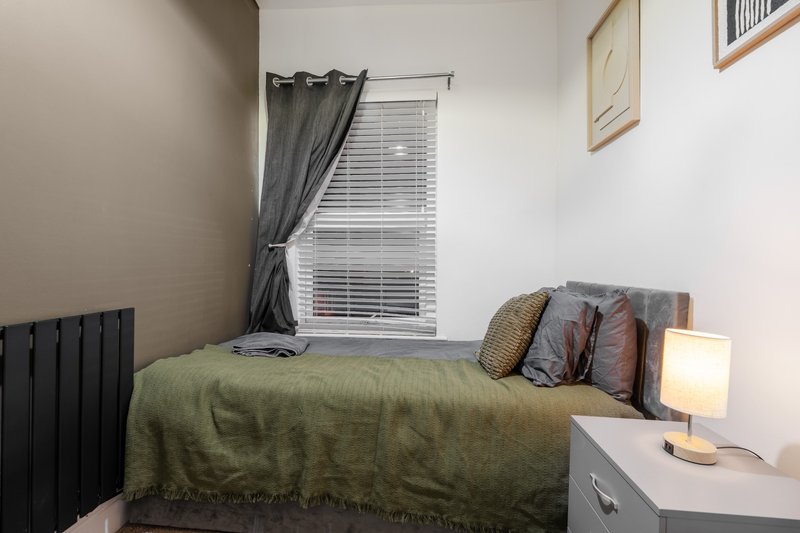 Compact bedroom with single bed, olive bedding, dark curtains, radiator and bedside lamp