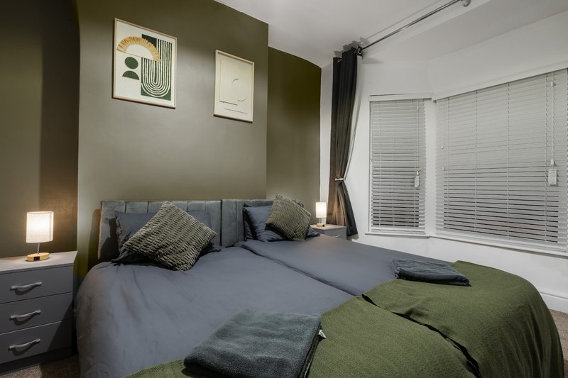 Modern bedroom with double bed, olive green walls, bedside lamp and sliding glass doors