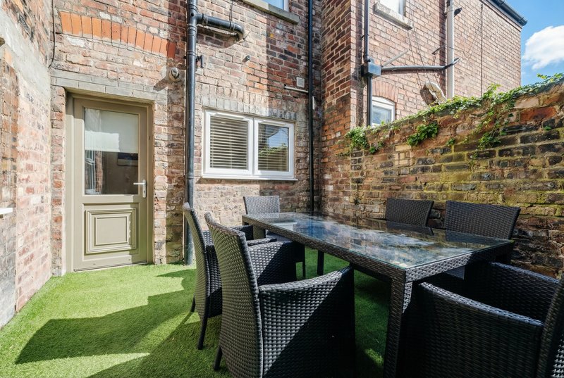 Brick townhouse patio with artificial grass, dining table, chairs and green door