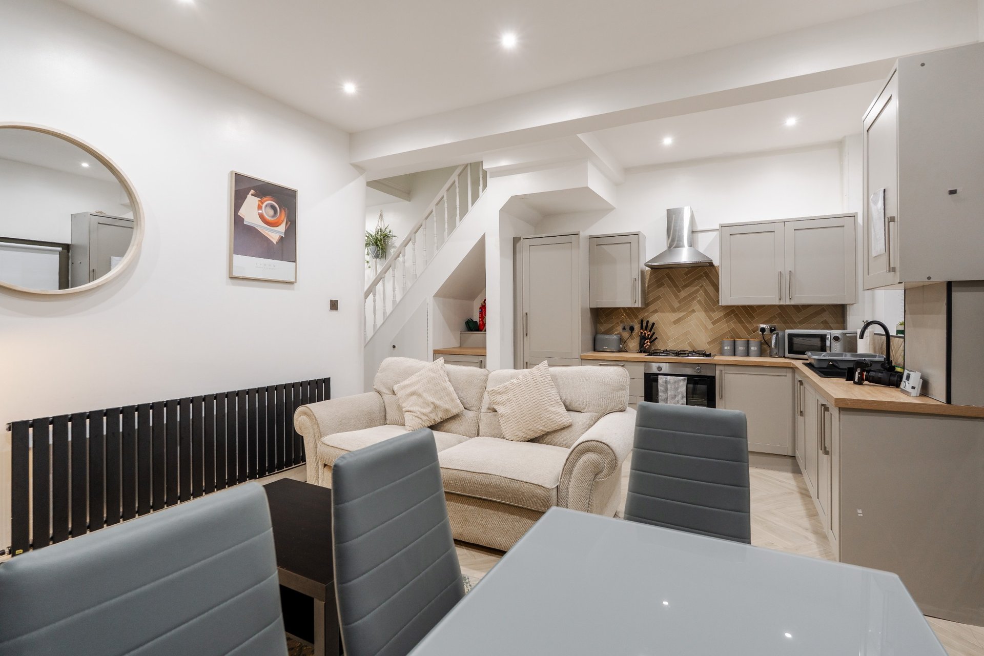 Open-plan living area with dining table, cream sofa, kitchen, and staircase to upper level