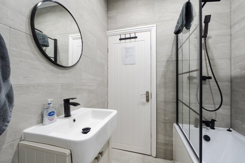 Modern bathroom with white sink, round mirror, shower enclosure and tiled walls