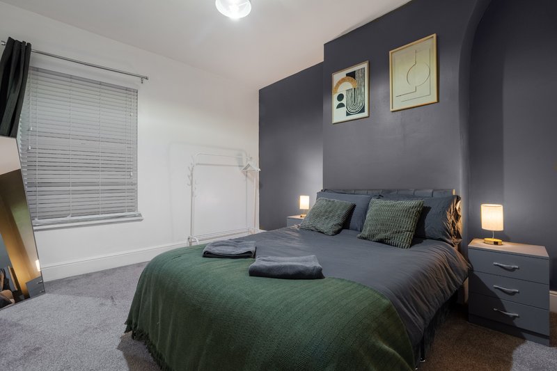Modern bedroom with dark feature wall, double bed with green bedding, bedside lamps and artwork