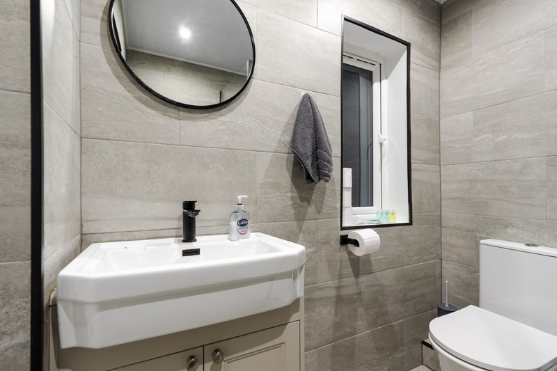 Modern bathroom with white sink, round mirror, toilet and tiled walls