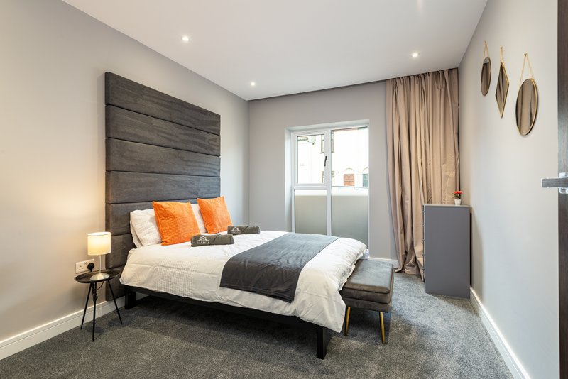 Modern bedroom with double bed, dark headboard, orange cushions, bedside lamp and window with curtains