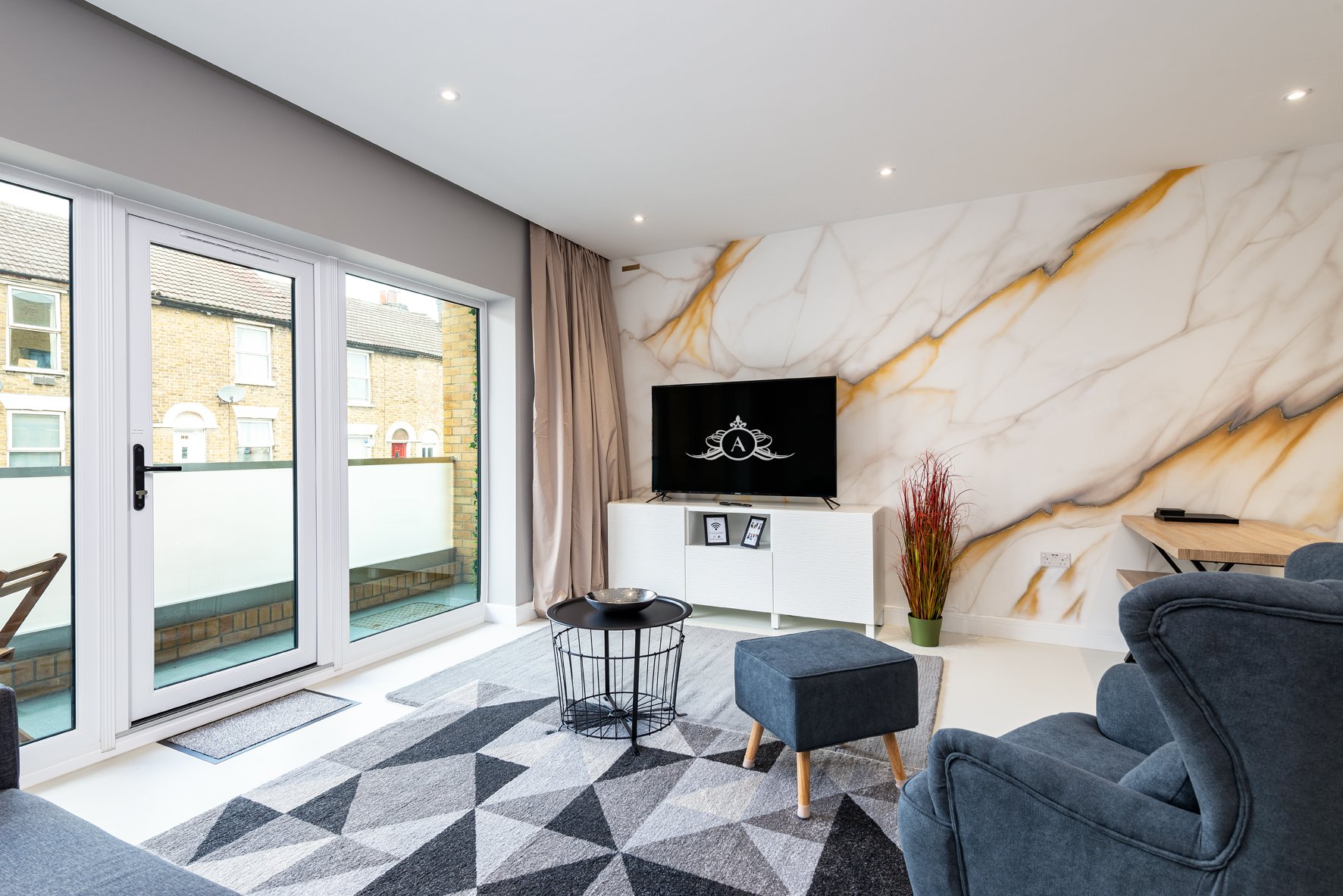 Modern living room with blue armchairs, marble feature wall, TV, and glass doors to balcony