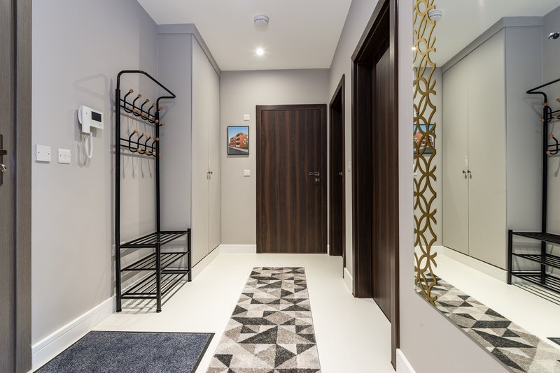 Modern hallway with light walls, geometric floor runner, wall-mounted coat racks and storage organizers