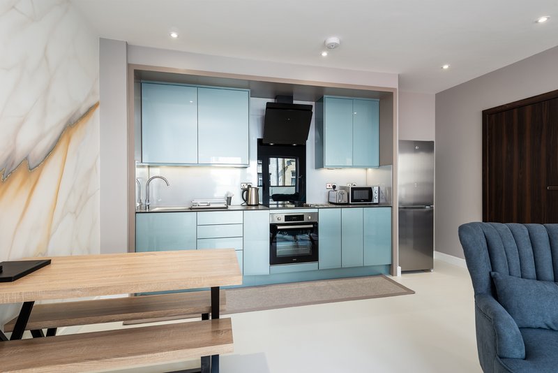 Modern open-plan kitchen and dining area with light blue cabinetry, wooden table, and blue upholstered chair