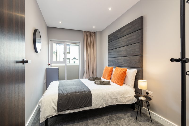 Modern bedroom with double bed, grey headboard, orange pillows, and bedside table lamp
